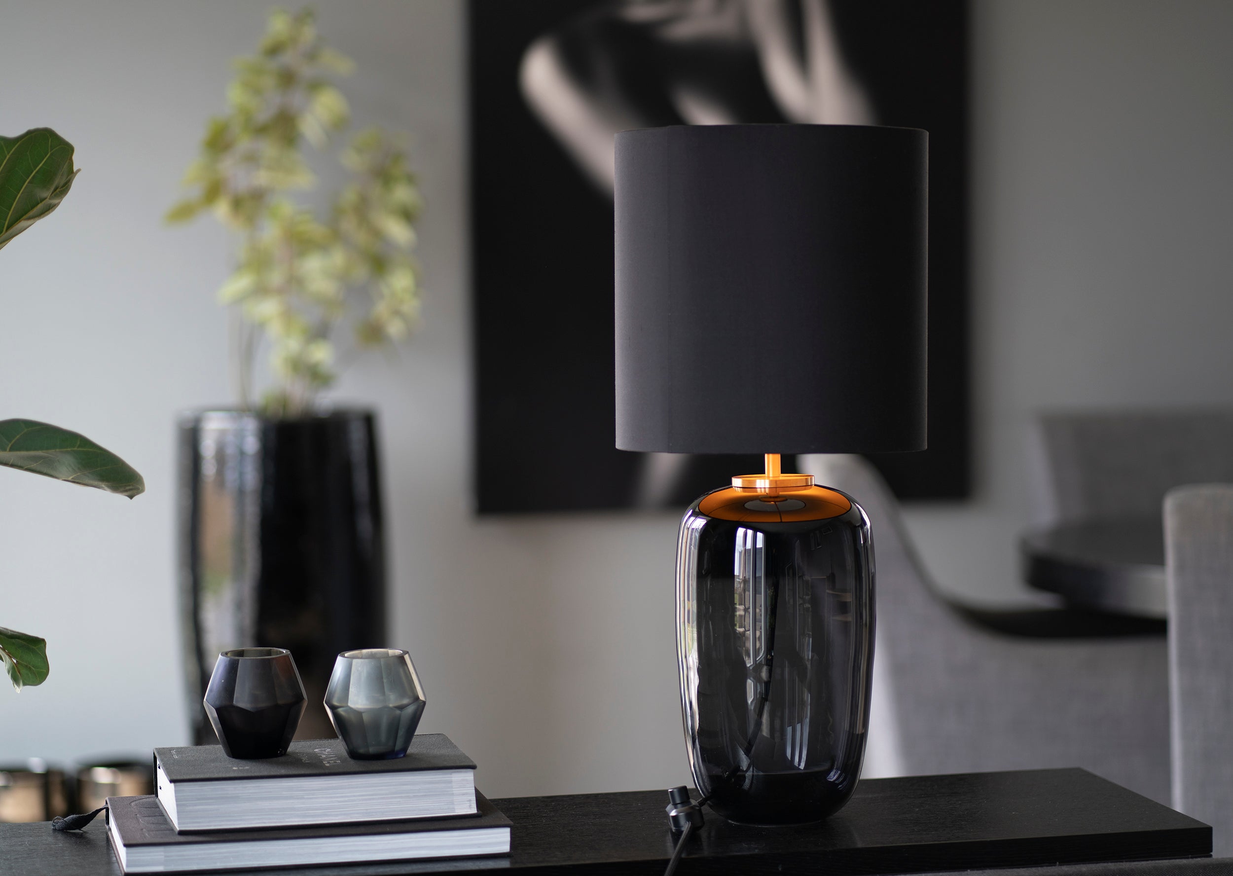 Vega bordlampe med røkgrå fot og svart skjerm i stue. Lampen er produsert av Hadeland Glassverk.