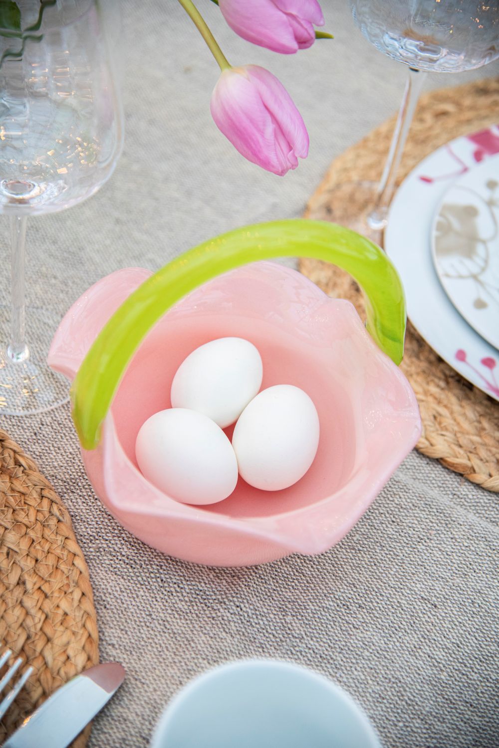 Rosa glasskurv med hank med egg på et dekket påskebord